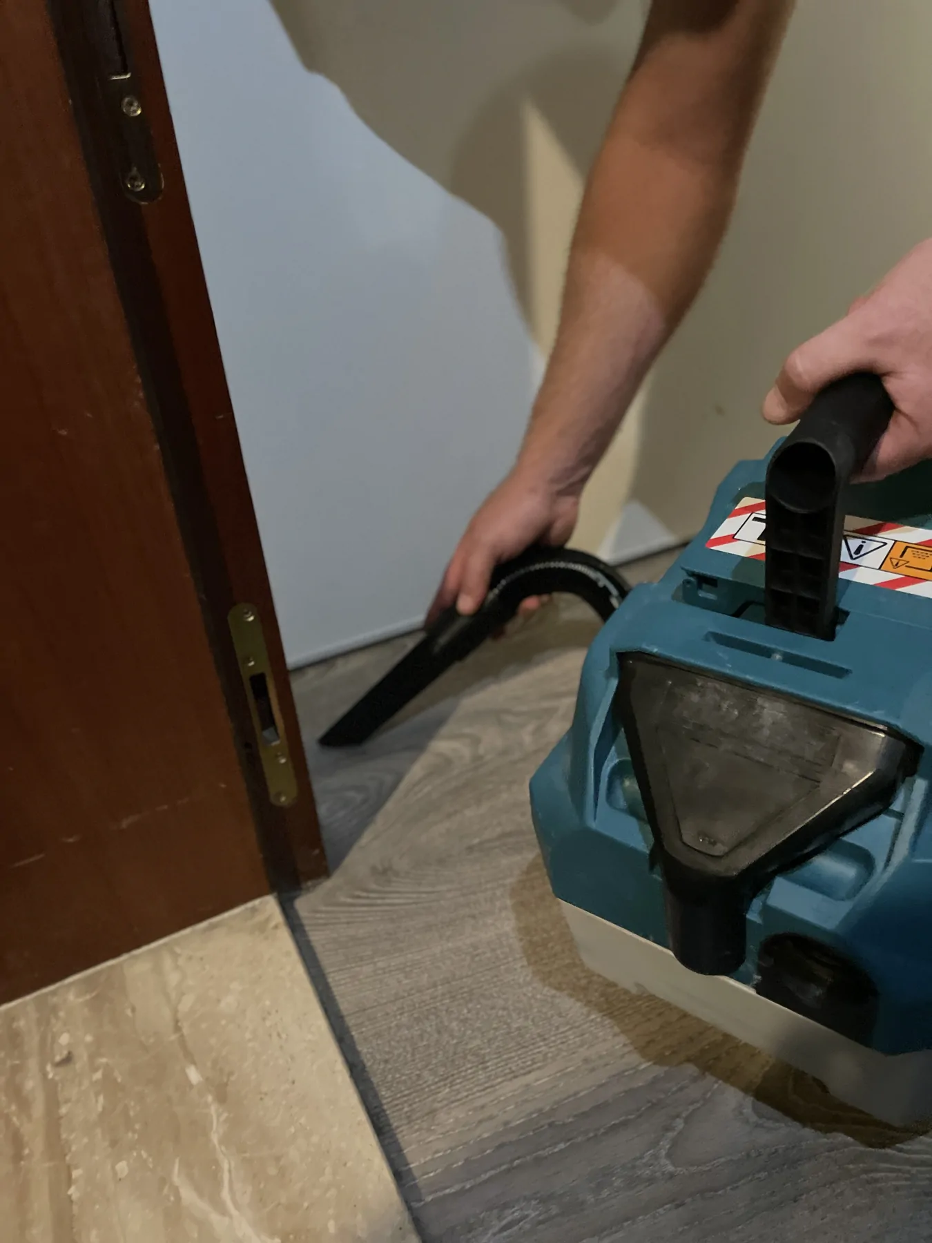 Une personne utilise l’embout d’un aspirateur au seuil d’une porte.