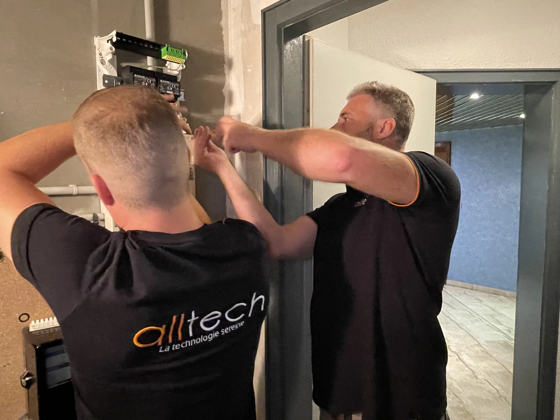 Deux intervenants en polo Alltech travaillent sur un coffret mural ouvert.
