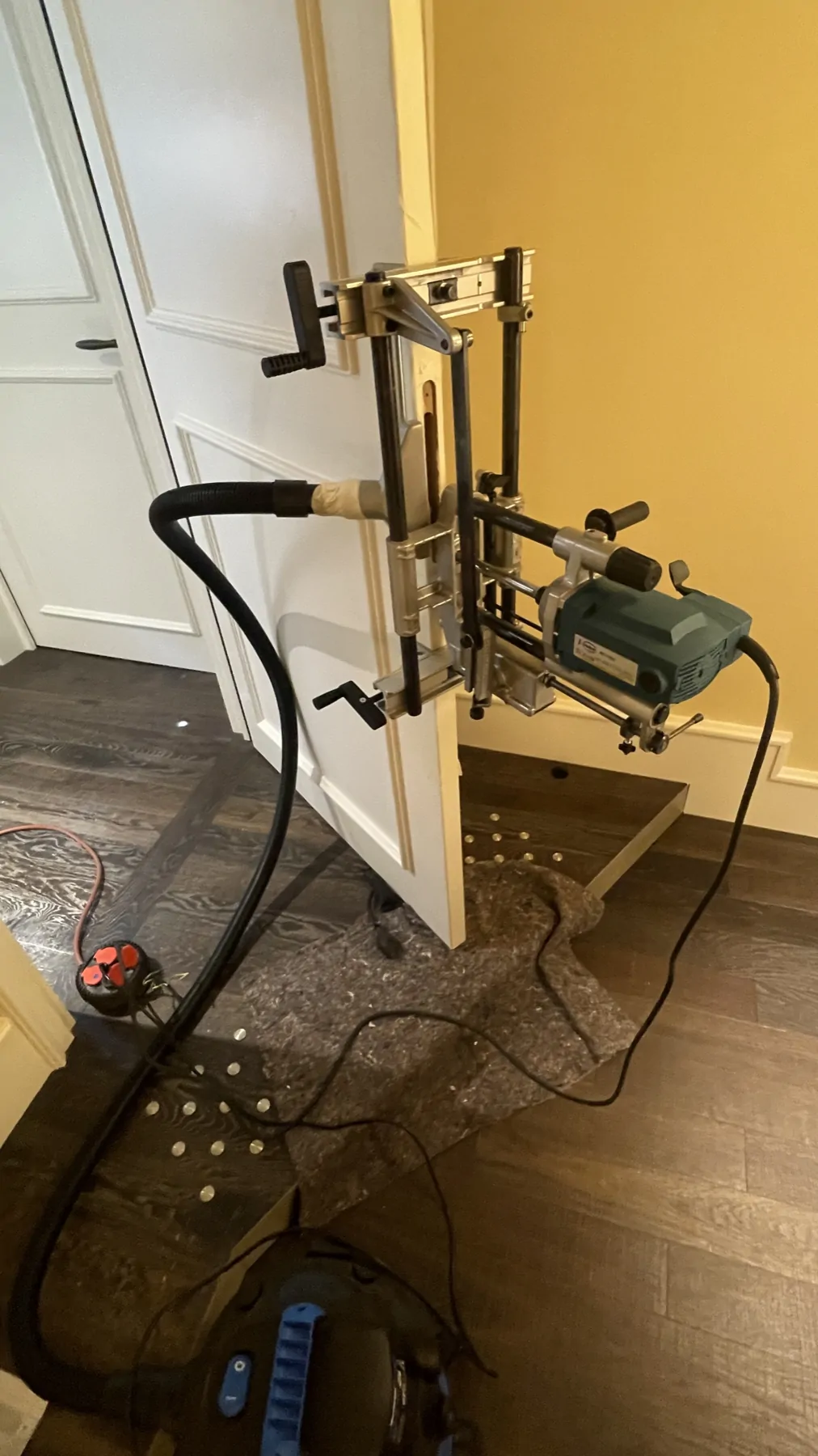 Outillage guidé fixé sur une porte, avec tuyau d’aspiration et protection au sol.