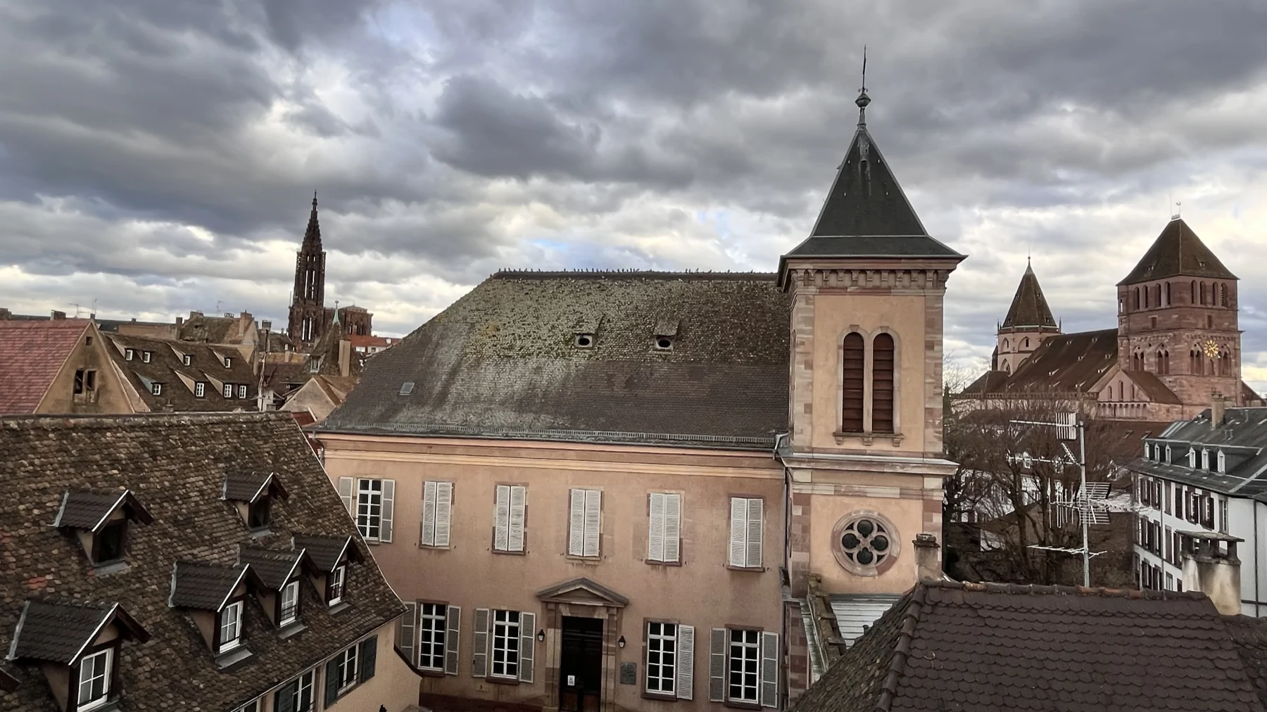 Toitures et bâtiments urbains vus depuis un point élevé sous un ciel nuageux.
